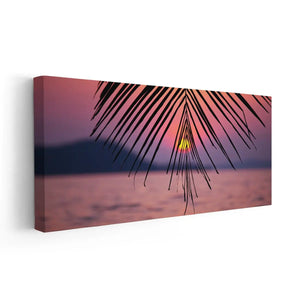 Beach wall art for living room featuring a dreamy ocean sunset framed by palm leaves in the foreground.