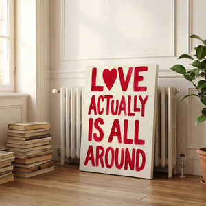 Gallery wrapped canvas with uneven hand-painted lines forming the phrase 'LOVE ACTUALLY IS ALL AROUND' in red on white.