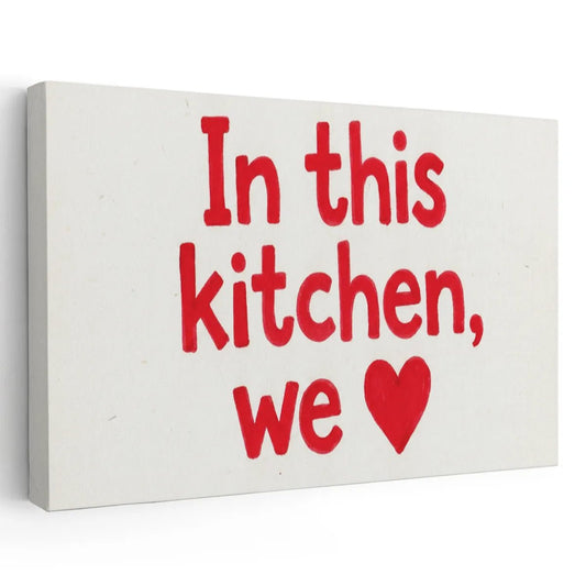 Bold canvas wall art featuring red text and a heart symbol reading 'In this kitchen, we ❤️' on a white background