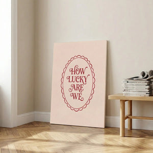 Vertical canvas art with centered phrase 'HOW LUCKY ARE WE' in red, enclosed in a retro oval border on a neutral background