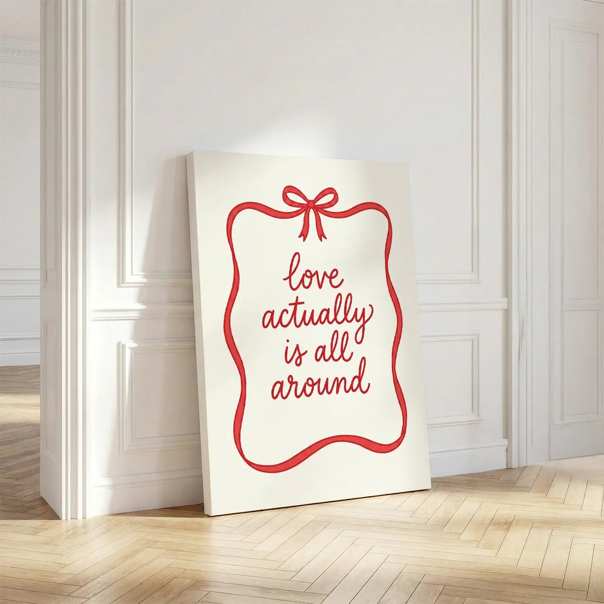 Canvas wall decor with centered red cursive typography enclosed by a single red ribbon and bow on a clean white backdrop