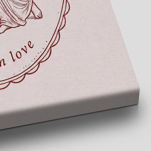 Romantic canvas wall art showing a winged figure embracing a draped partner within a detailed oval border and muted burgundy tones.