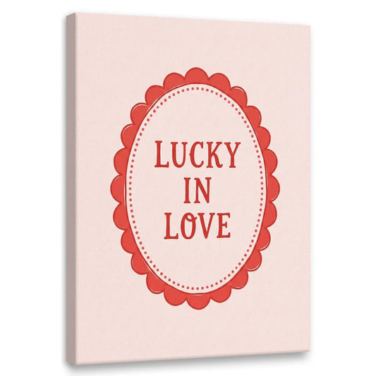 Minimalist canvas wall art featuring red 'LUCKY IN LOVE' text inside a scalloped oval frame on a light pink background